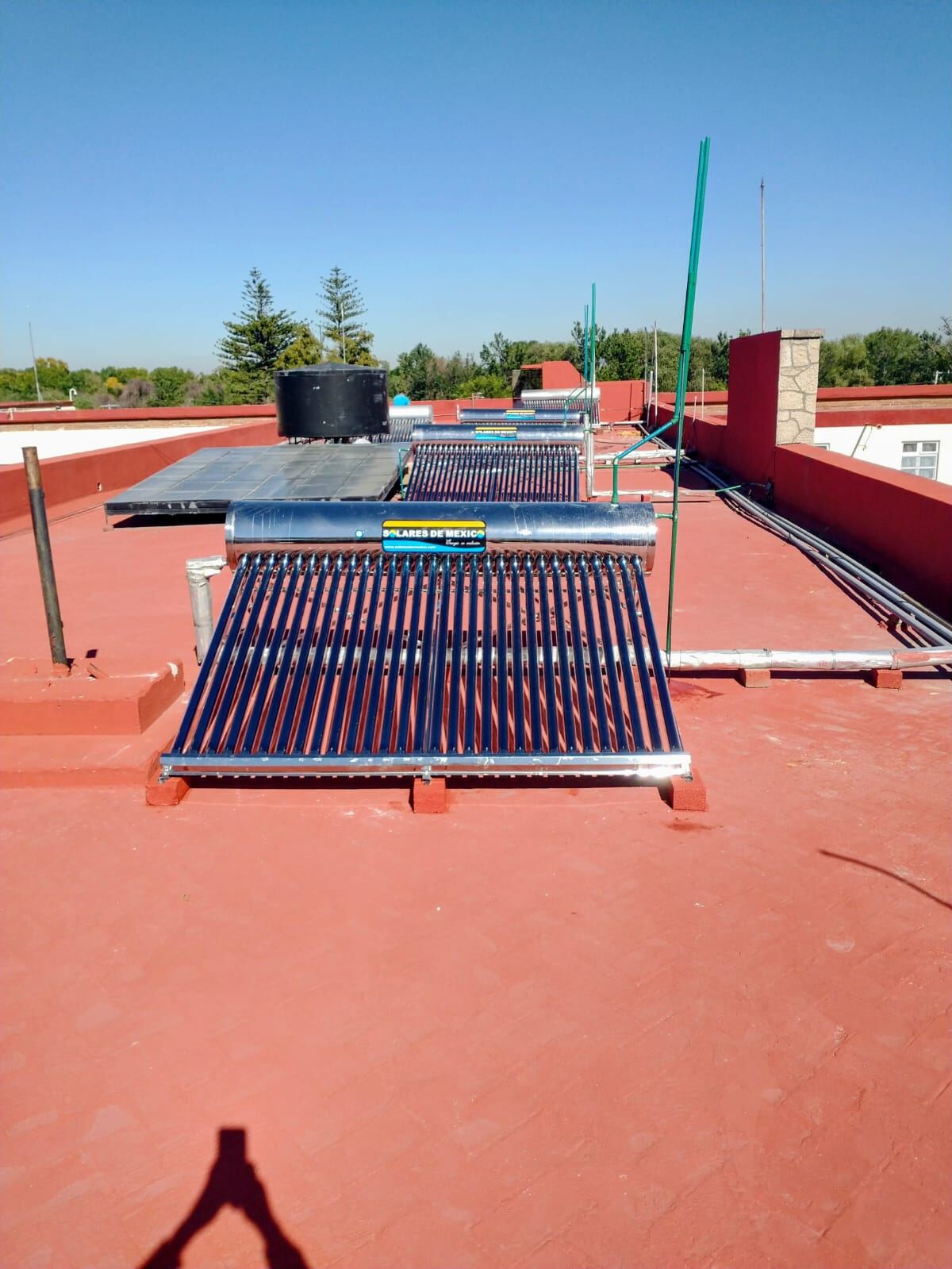 Calentador solar instalado sobre una azotea roja con tinaco elevado